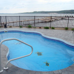 Bermuda freeform fiberglass inground Latham pool with curved shape, built-in entry steps, and stamped-concrete patio in a landscaped backyard by Calm Water Pools 