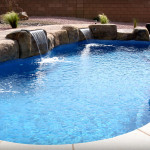 Laguna freeform inground fiberglass pool with curved organic shape, light blue water and concrete patio in a landscaped backyard