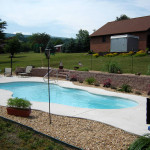 Laguna freeform inground fiberglass pool with smooth curved design, built-in entry steps and light concrete patio in a residential backyard