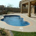 Laguna freeform inground fiberglass pool with lagoon-style curves, light concrete pool deck and landscaped backyard seating area