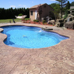 Laguna freeform inground fiberglass pool with light blue water, stamped concrete deck and rock landscaping in a suburban backyard