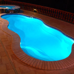 Laguna freeform inground fiberglass pool with curved organic shape, light concrete pool deck and backyard lounging area