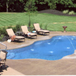 Laguna freeform inground fiberglass pool with flowing curved design, light blue water and surrounding concrete patio in a landscaped backyard