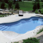 Laguna freeform inground fiberglass pool with flowing curved design, built-in entry steps and concrete patio in a landscaped backyard
