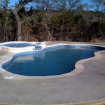 Laguna freeform inground fiberglass pool with curved lagoon-style design, built-in entry steps and concrete pool deck in a landscaped backyard