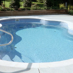 Laguna freeform inground fiberglass pool with curved lagoon-style shape, built-in entry steps and concrete deck in a landscaped backyard
