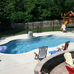 Laguna freeform inground fiberglass pool with curved design, shallow entry steps and concrete patio in a landscaped residential backyard