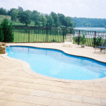 Laguna freeform inground fiberglass swimming pool with curved organic shape, light concrete pool deck and landscaped backyard setting