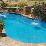 Laguna freeform inground fiberglass pool with flowing curved shape, built-in entry steps and concrete pool deck in a landscaped backyard