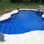 Laguna freeform inground fiberglass pool with flowing curved design, built-in entry steps and concrete pool deck in a private backyard