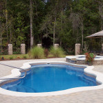 Laguna freeform inground fiberglass pool with curved organic shape, built-in entry steps and textured concrete deck in a private backyard