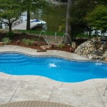 Laguna Freeform inground fiberglass pool with curved freeform shape, built-in entry steps and surrounding patio in a landscaped backyard