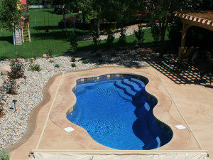 Bermuda medium inground fiberglass Latham pool with bright blue water and stamped-concrete patio in a landscaped backyard by Calm Water Pools 