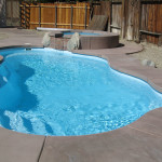 Bermuda medium inground fiberglass Latham pool with freeform shape, built-in entry steps, and stamped-concrete patio in a landscaped backyard by Calm Water Pools 