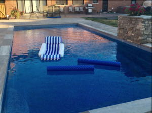 Olympia classic inground fiberglass Latham pool with wide entry steps and tanning ledge in a landscaped backyard by Calm Water Pools